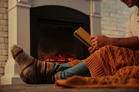 Man warming up with orange plaid while reading book at fireplace, closeupの写真素材