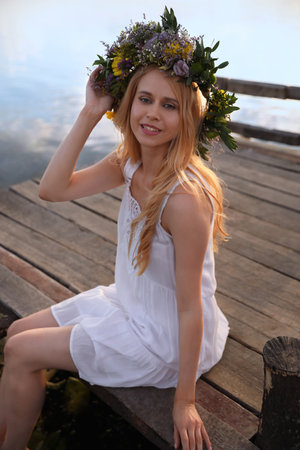Young woman wearing wreath made of beautiful flowers on pier near riverの写真素材