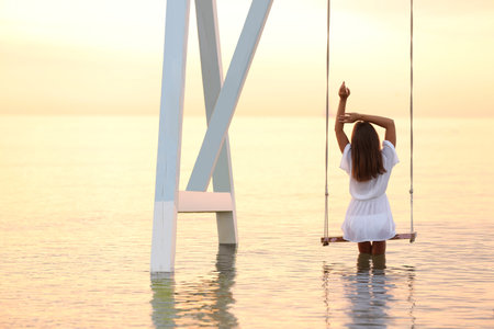 Young woman enjoying sunrise on swing over waterの写真素材