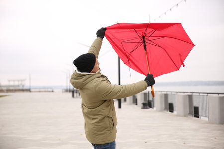 Man with red umbrella caught in the thick of wind outdoorsの写真素材