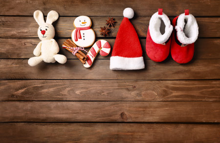 Cute baby booties, small Santa hat, gingerbreads and toy rabbit on wooden background, flat lay. Space for textの写真素材