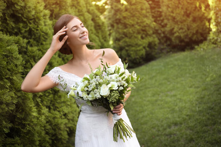 Gorgeous bride in beautiful wedding dress with bouquet outdoorsの写真素材