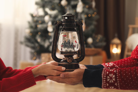 Couple in Santa hats holding snow globe in room with Christmas tree, closeupの写真素材