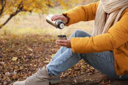 Woman with flask sitting on ground outdoors, closeupの写真素材