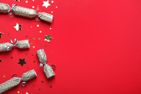Open and closed Christmas crackers with shiny confetti on red background, flat lay. Space for textの写真素材