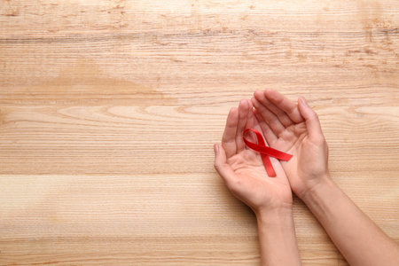 Woman holding red awareness ribbon on wooden background, top view with space for text. World AIDS...