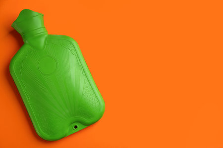 Green rubber hot water bottle on orange background, top view. Space for textの写真素材