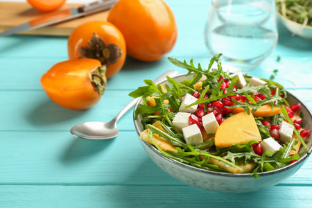 Delicious persimmon salad with pomegranate and arugula on light blue wooden tableの写真素材