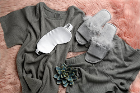 Pair of fluffy slippers, pajamas and sleeping eye mask on fuzzy carpet, flat lay. Comfortable home outfitの写真素材