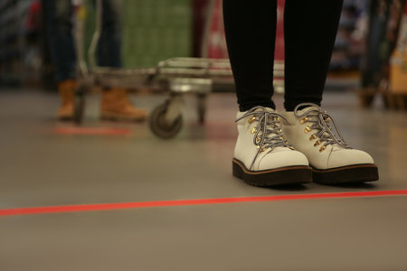 Woman standing behind taped floor marking in store for social distance, closeup. Preventive measure during coronavirus pandemicの写真素材