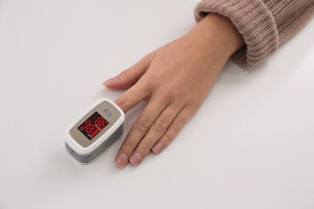 Woman measuring oxygen level with modern fingertip pulse oximeter at white table, top viewの写真素材