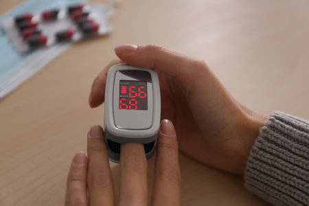 Woman measuring oxygen level with modern fingertip pulse oximeter at wooden table, closeup