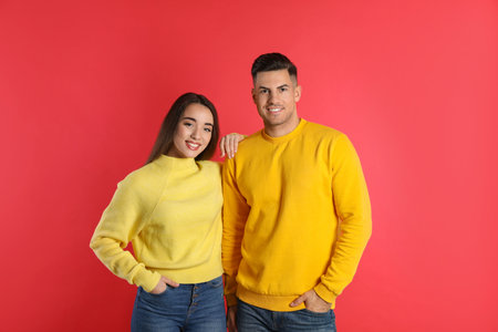 Happy couple wearing yellow warm sweaters on red backgroundの写真素材