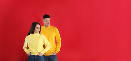 Happy couple wearing yellow warm sweaters on red background. Space for textの写真素材