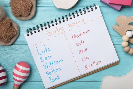 Notebook with different baby names and toys on light blue wooden table, flat layの写真素材