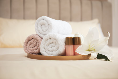Rolled clean towels, flower and shampoo bottles on bedの写真素材