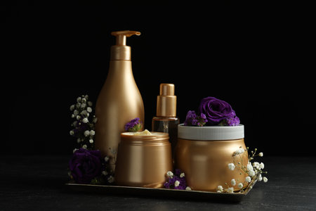 Set of hair cosmetic products and flowers on stone table against black backgroundの写真素材
