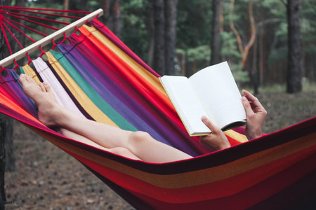 Woman with book relaxing in hammock outdoors on summer day, closeup