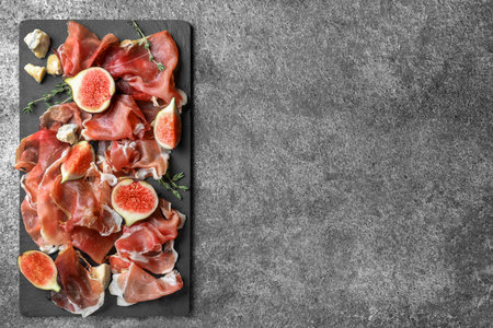 Delicious ripe figs and prosciutto served on grey table, flat lay. Space for textの写真素材