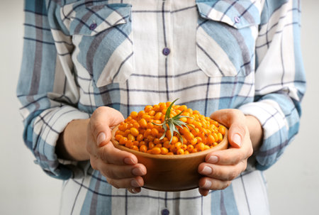 Woman holding bowl with fresh ripe sea buckthorn on light background, closeupの写真素材