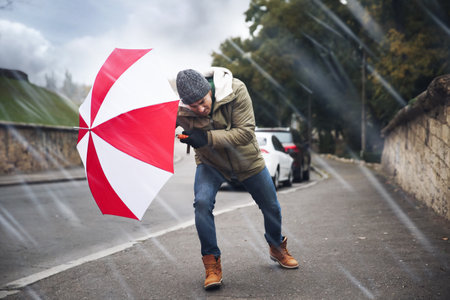 Man with colorful umbrella caught in gust of wind on streetの写真素材