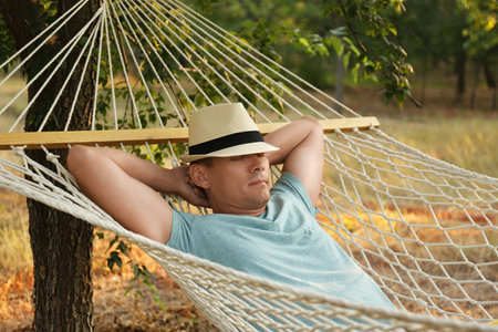 Man with hat resting in comfortable hammock at green gardenの写真素材
