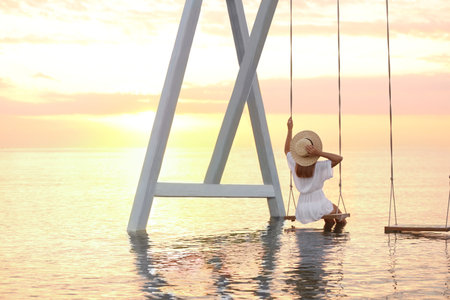 Young woman enjoying sunrise on swing over waterの写真素材