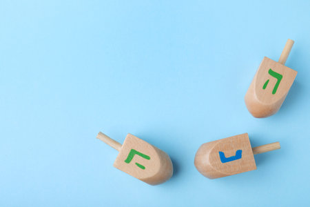 Hanukkah traditional dreidels with letters He and Nun on light blue background, flat lay. Space for textの写真素材