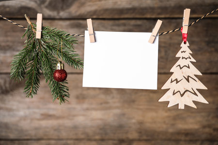 Blank Christmas card and festive decor on rope against wooden background. Space for textの写真素材