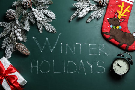 Flat lay composition of Christmas sock, decorations, gift box and alarm clock on school blackboard with phrase Winter Holidaysの写真素材