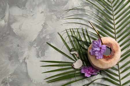 Young peeled coconut with straw, tropical leaf and flowers on grey table, flat lay. Space for textの写真素材