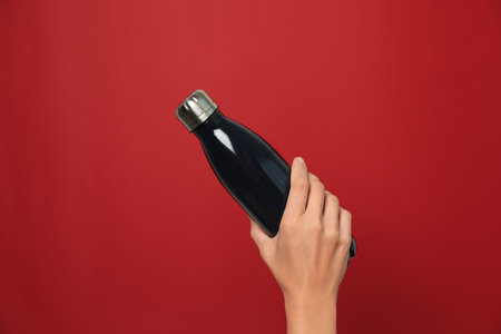 Woman holding modern dark thermo on red background, closeupの写真素材
