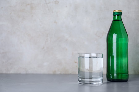 Glass and bottle with water on table against grey background, space for textの写真素材