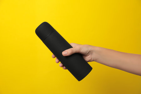 Woman holding modern black thermo on yellow background, closeupの写真素材