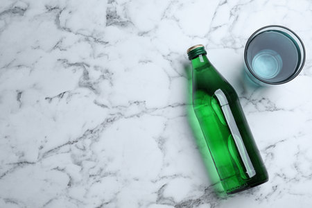 Glass and bottle with water on white marble background, flat lay. Space for textの写真素材