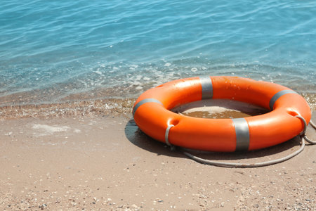 Orange life buoy on sand near the sea. emergency rescue equipment