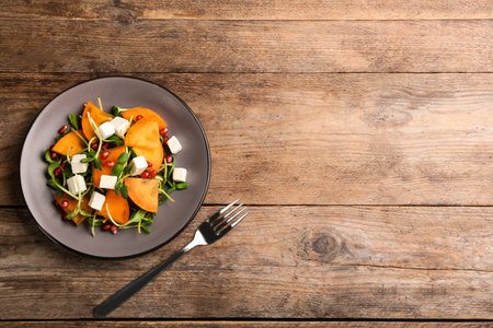 Delicious persimmon salad served on wooden table, flat lay. Space for textの写真素材