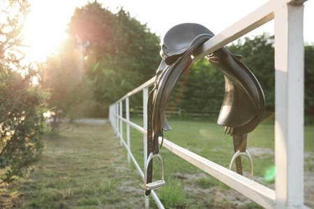 Leather horse saddle on wooden fence outdoors