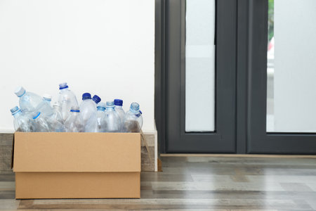 Cardboard box with used plastic bottles near entrance door in hallway. recycling problemの写真素材