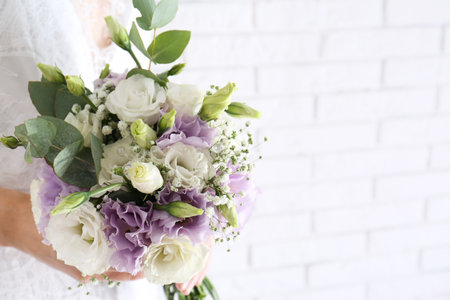 Bride holding beautiful bouquet with Eustoma flowers near brick wall, closeup. Space for textの写真素材