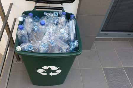 Many used plastic bottles in trash bin near entrance outdoors. recycling problem