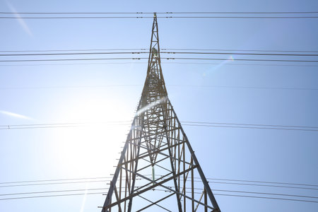 High voltage tower with electricity transmission power lines against blue sky, low angle view