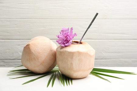 Young peeled coconuts with straw, palm leaf and flower on white wooden tableの写真素材