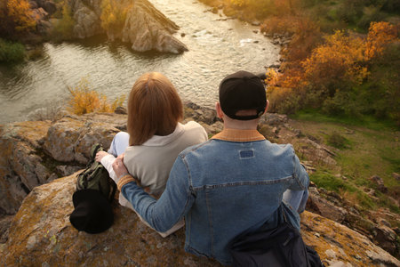Couple of hikers with travel backpacks sitting on steep cliff, above viewの写真素材