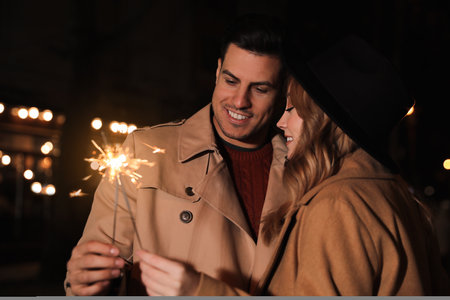 Couple in warm clothes holding burning sparklers at nightの写真素材