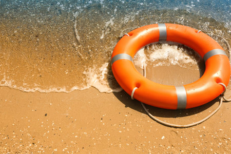 Orange life buoy on sand near the sea. emergency rescue equipment