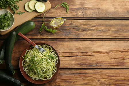 Tasty zucchini pasta with arugula and ingredients on wooden table, flat lay. Space for textの写真素材