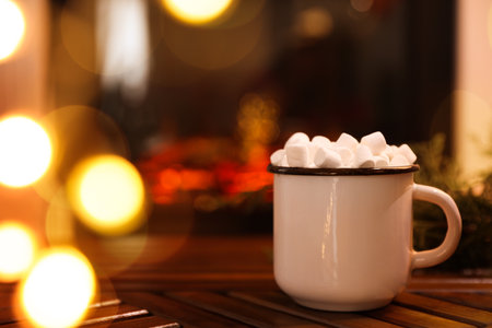 Cup of hot drink with marshmallows on wooden table near fireplace at home. Space for textの写真素材