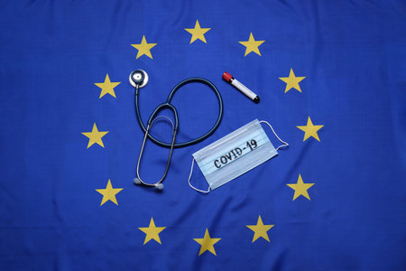 Stethoscope, medical mask with word COVID-19 and test tube on flag of European Union, flat layの写真素材