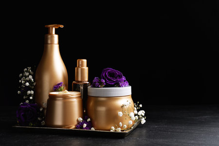 Set of hair cosmetic products and flowers on stone table against black background. Space for textの写真素材